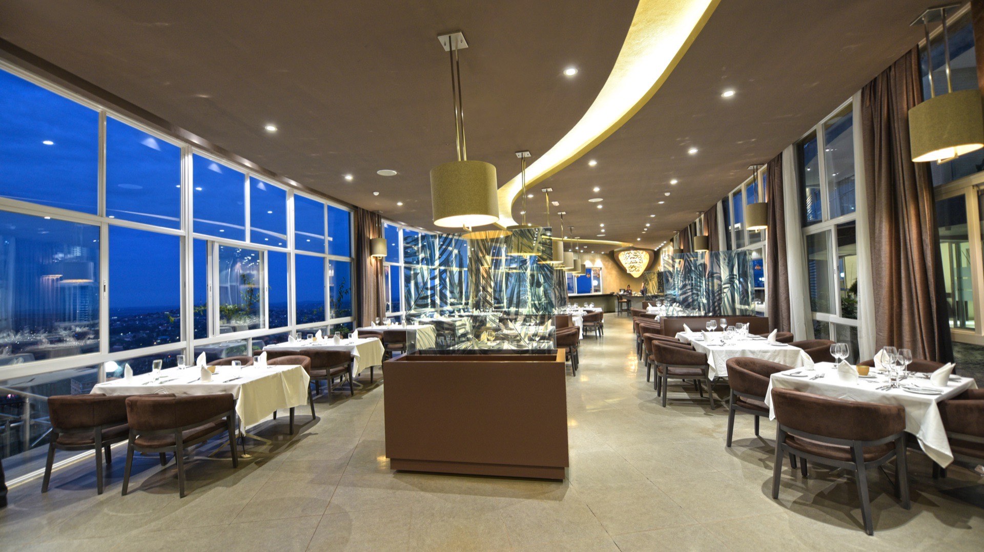 Chapter Two Restaurant dining room in the evening, with frosted palm-leaf glass dividers and floor-to-ceiling windows over the Kampala skyline
