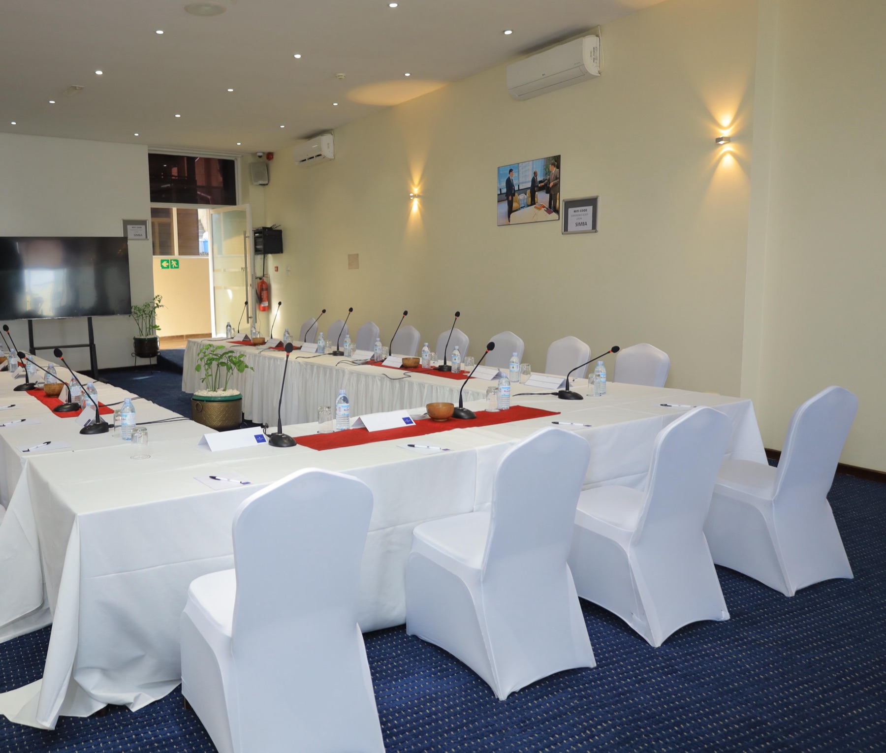 A conference room at Skyz Hotel Kampala set up in U-shape style with round-back chairs, red table runners and blue carpet