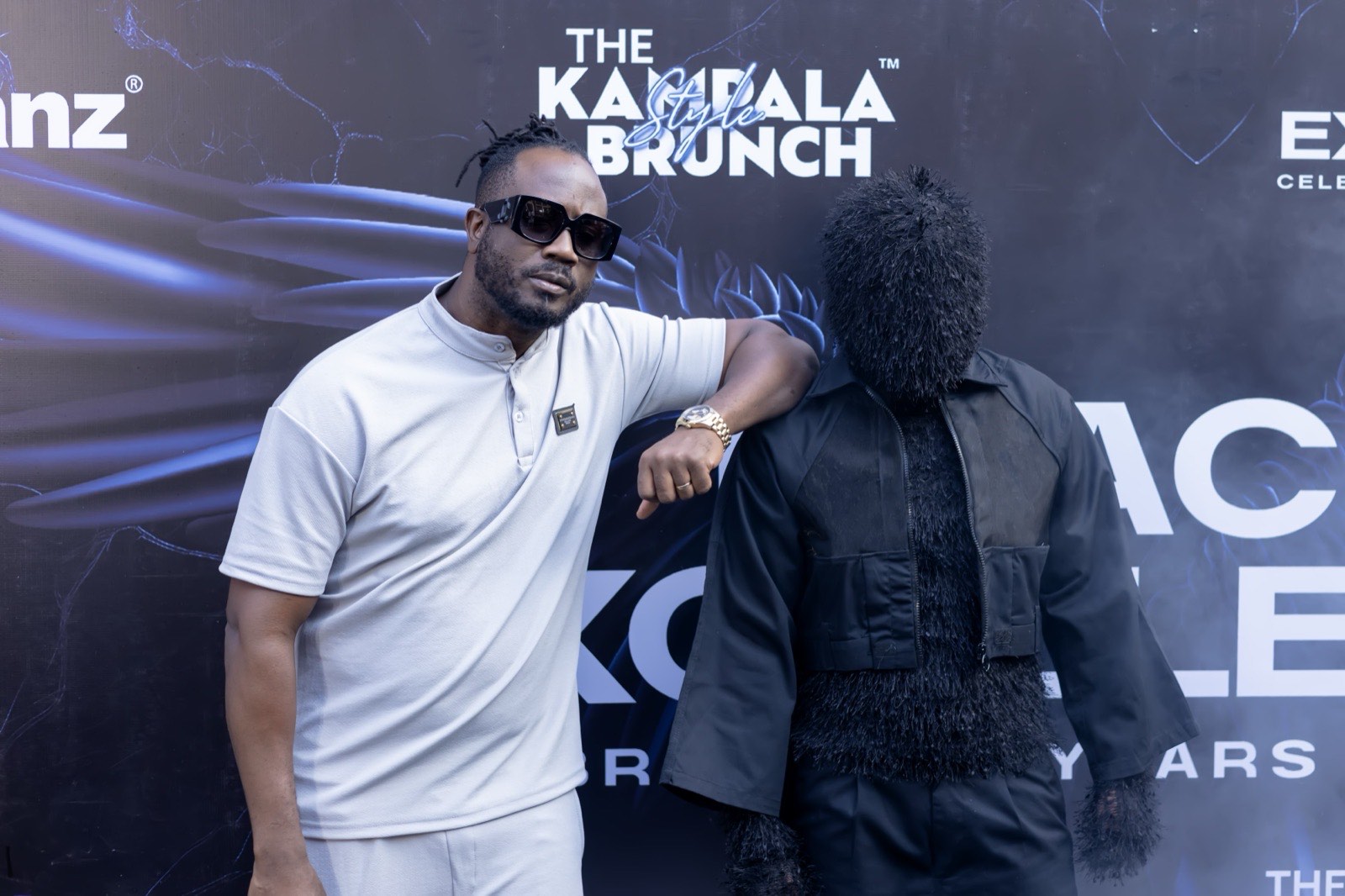 A guest poses beside a costumed display at The Kampala Style Brunch branded backdrop, October 2024