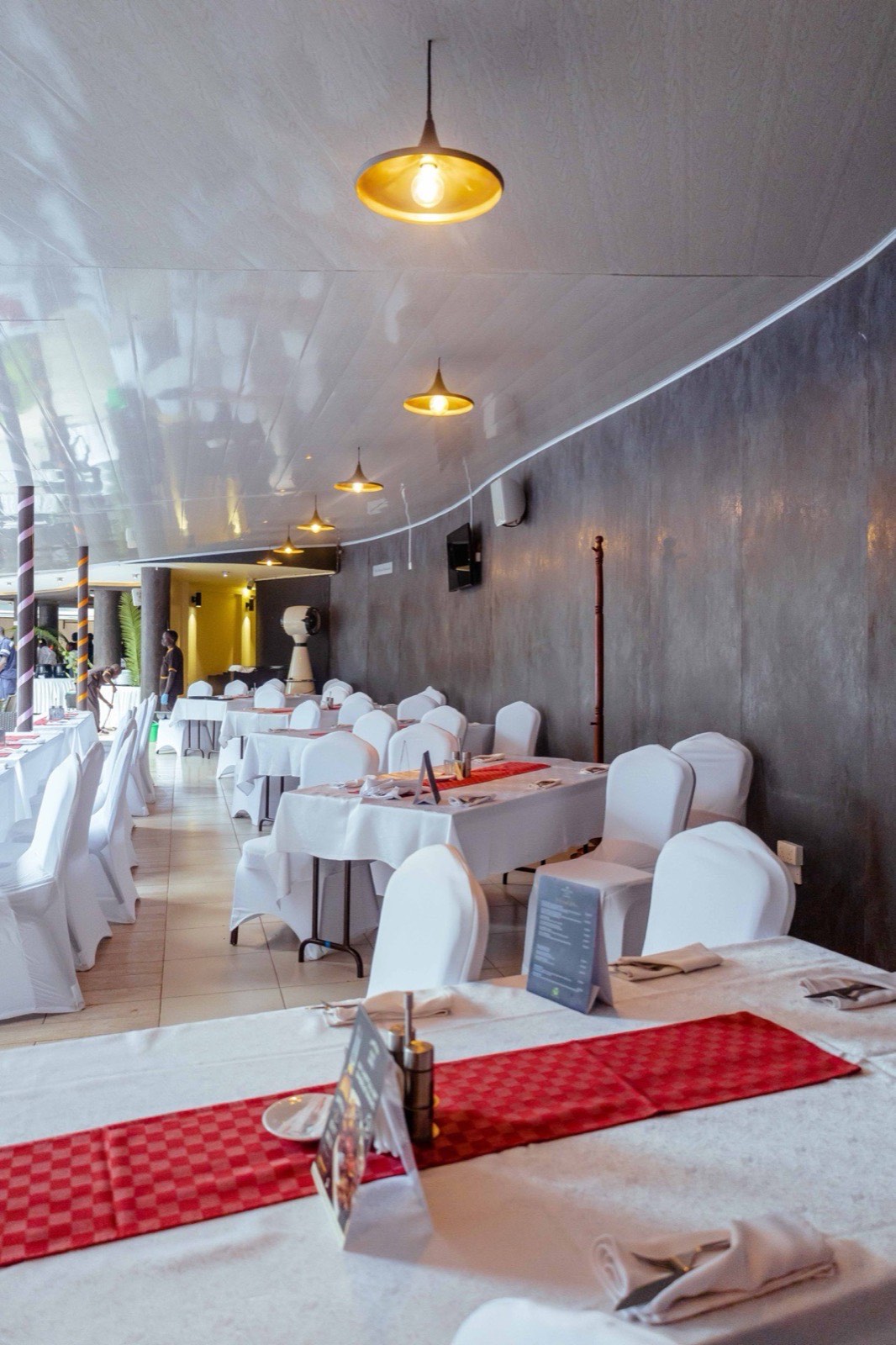 The covered terrace section of the Tropicanna Poolside Restaurant, dressed with white linens and pendant lighting